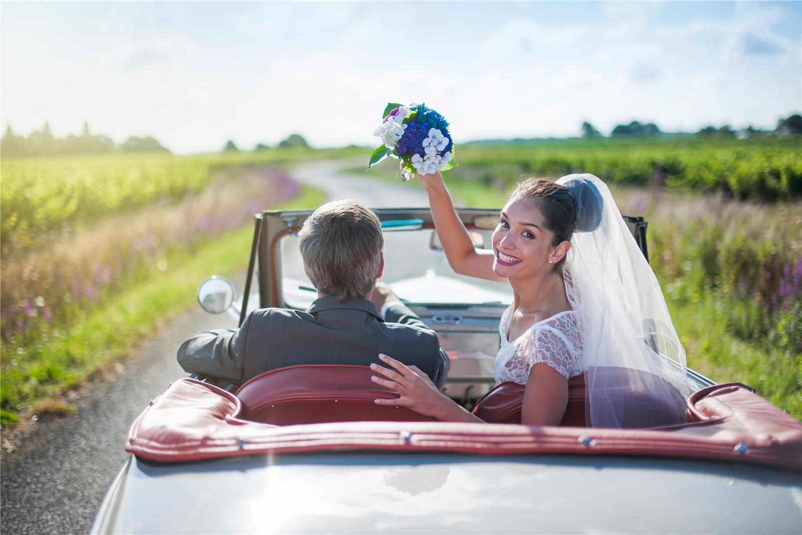 חתן וכלה נוסעים ברכב כאשר הכלה מנופפת בזר פרחים לאחר טקס החתונה האזרחית
